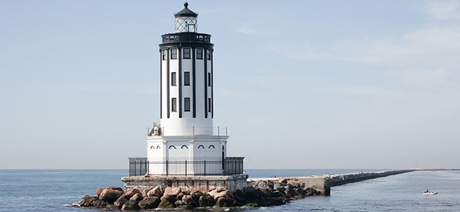 Lighthouse surrounded by rocks & boat in the ocean waters